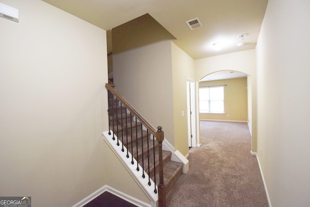 stairway with arched walkways, carpet, visible vents, and baseboards