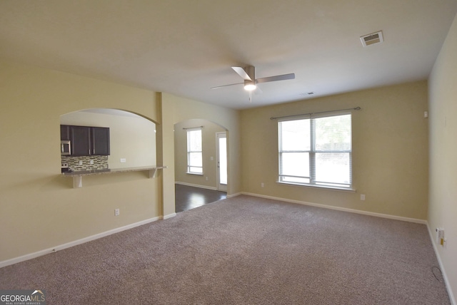 unfurnished room with dark colored carpet, arched walkways, baseboards, visible vents, and a ceiling fan