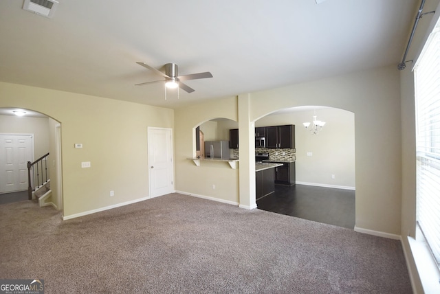 unfurnished living room featuring dark colored carpet, visible vents, arched walkways, baseboards, and ceiling fan with notable chandelier
