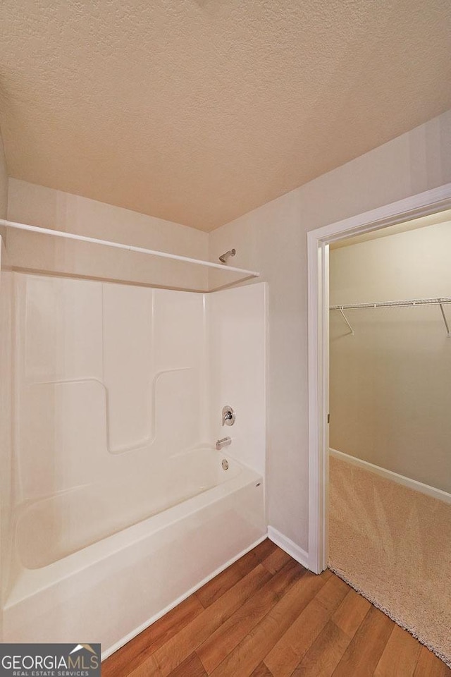 full bath with wood finished floors, a walk in closet, baseboards,  shower combination, and a textured ceiling