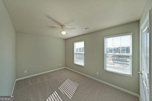 carpeted spare room featuring baseboards, visible vents, a textured ceiling, and ceiling fan