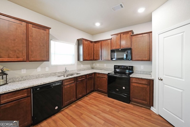 kitchen with light stone counters, a sink, black appliances, light wood finished floors, and visible vents