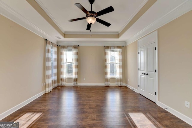 unfurnished room featuring a ceiling fan, a raised ceiling, dark wood finished floors, baseboards, and ornamental molding
