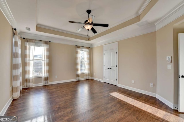 empty room featuring ceiling fan, a tray ceiling, ornamental molding, dark wood-type flooring, and visible vents
