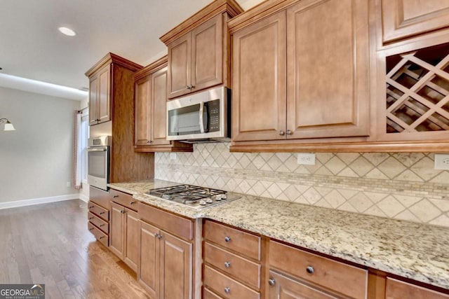 kitchen with light stone counters, light wood-style floors, decorative backsplash, and stainless steel appliances
