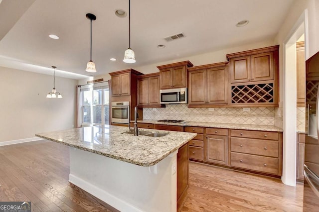 kitchen with a sink, light wood-type flooring, backsplash, appliances with stainless steel finishes, and visible vents