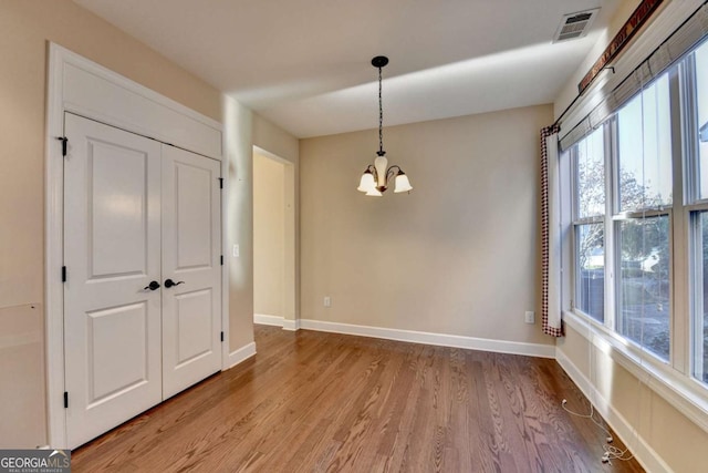 unfurnished dining area featuring a chandelier, light wood-style flooring, visible vents, and baseboards