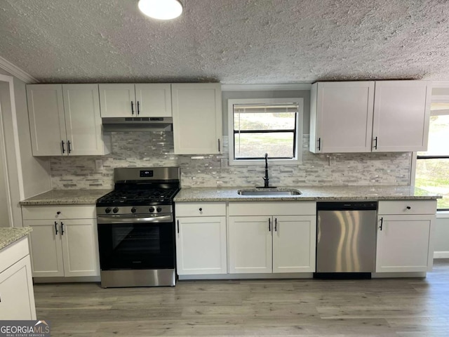 kitchen with a textured ceiling, appliances with stainless steel finishes, under cabinet range hood, and a sink