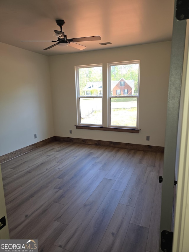 unfurnished room with a ceiling fan, visible vents, dark wood-style flooring, and baseboards