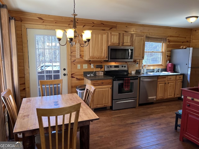 kitchen featuring an inviting chandelier, wood walls, dark countertops, appliances with stainless steel finishes, and dark wood finished floors