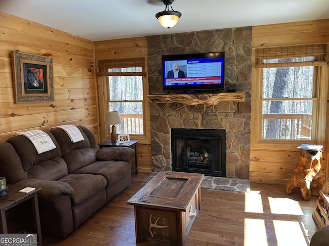 living room with wooden walls, wood finished floors, and a stone fireplace