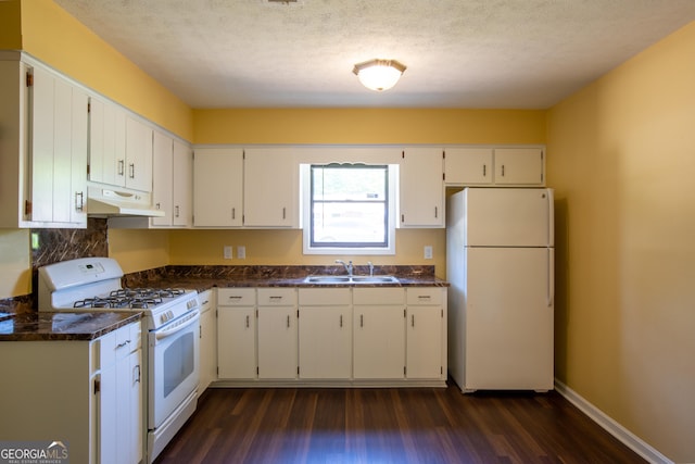 kitchen featuring under cabinet range hood, dark countertops, a sink, dark wood-type flooring, and white appliances