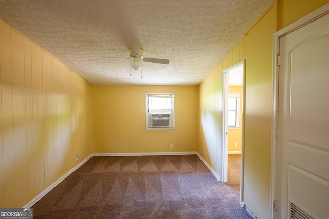 spare room featuring a ceiling fan, a textured ceiling, wooden walls, dark carpet, and baseboards
