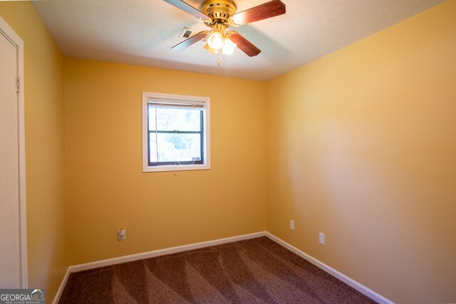 spare room with baseboards, a ceiling fan, dark colored carpet, and visible vents