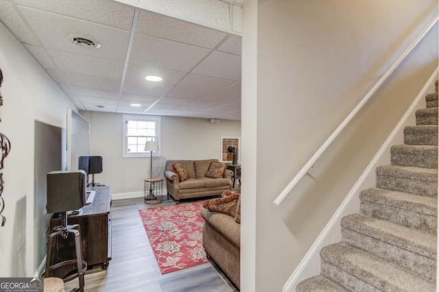 living area featuring a paneled ceiling, wood finished floors, baseboards, and a wood stove
