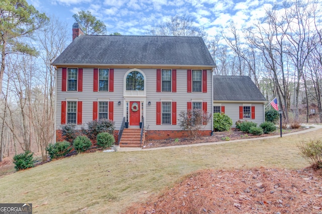 colonial-style house with a chimney, concrete driveway, a garage, a shingled roof, and a front yard