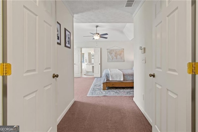 bedroom with ensuite bathroom, a textured ceiling, visible vents, carpet flooring, and baseboards