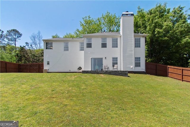 back of property with a fenced backyard, a chimney, and a yard