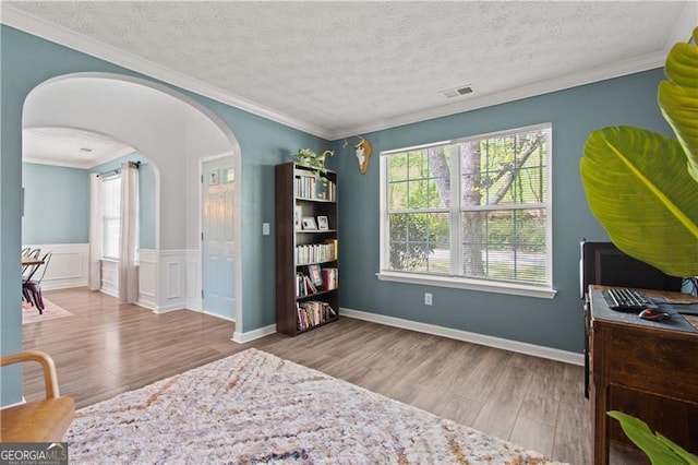 bedroom featuring crown molding, arched walkways, visible vents, and wood finished floors