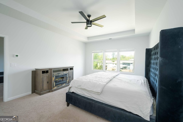 carpeted bedroom featuring ceiling fan, baseboards, a tray ceiling, and a fireplace