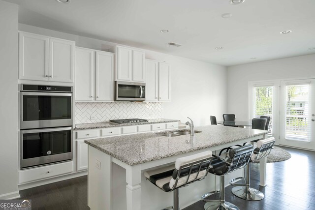 kitchen with white cabinets, a sink, light stone countertops, appliances with stainless steel finishes, and dark wood-style flooring