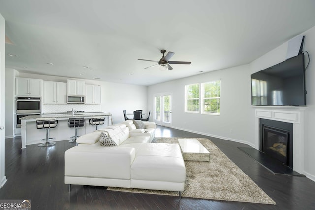 living room with dark wood-type flooring, a glass covered fireplace, a ceiling fan, and baseboards