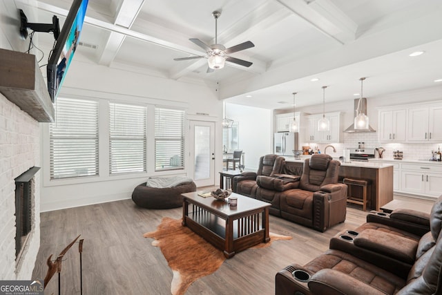 living area featuring a fireplace, light wood finished floors, beamed ceiling, and ceiling fan