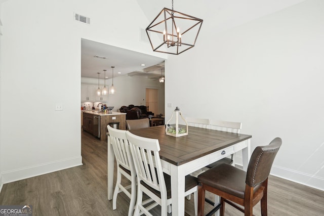 dining area with wood finished floors, a towering ceiling, baseboards, a notable chandelier, and visible vents