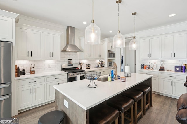 kitchen with dark wood finished floors, decorative backsplash, appliances with stainless steel finishes, wall chimney range hood, and a breakfast bar area