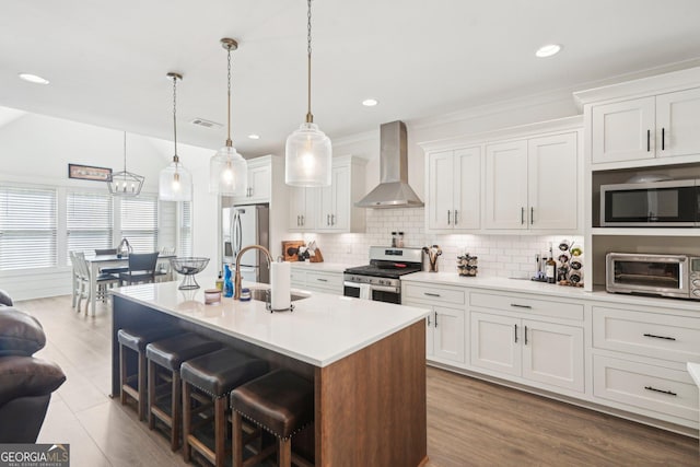 kitchen featuring a sink, stainless steel appliances, a kitchen bar, wall chimney exhaust hood, and white cabinetry