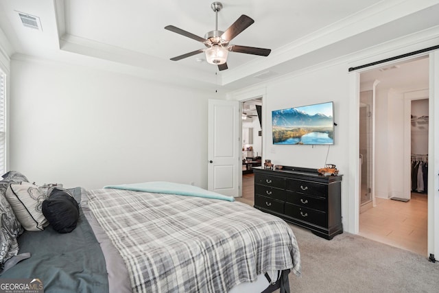 bedroom with a tray ceiling, visible vents, light colored carpet, ceiling fan, and a walk in closet