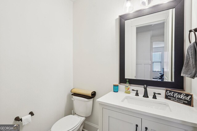 half bathroom featuring baseboards, toilet, and vanity