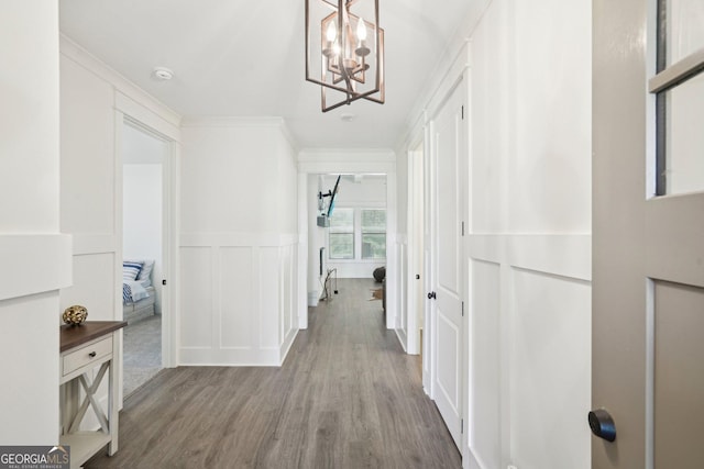 hallway featuring a wainscoted wall, a notable chandelier, wood finished floors, a decorative wall, and ornamental molding