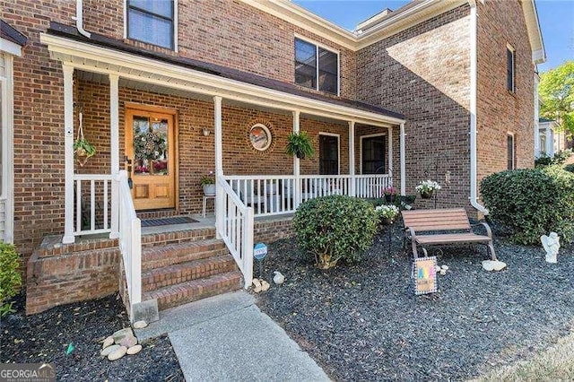 view of exterior entry featuring covered porch and brick siding