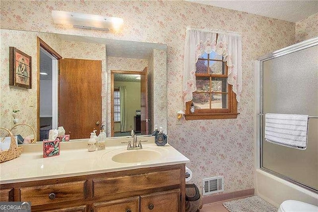 bathroom with visible vents, vanity, baseboards, wallpapered walls, and combined bath / shower with glass door
