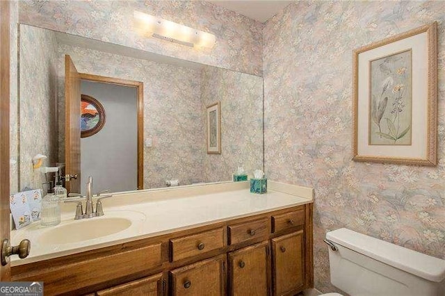 bathroom with vanity, toilet, and wallpapered walls
