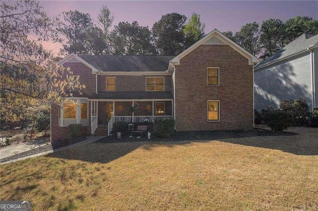 traditional home featuring brick siding, a front lawn, and covered porch