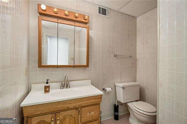 bathroom featuring toilet, visible vents, tile walls, and vanity