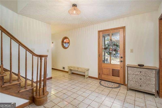 entrance foyer featuring baseboards, light tile patterned floors, and stairway