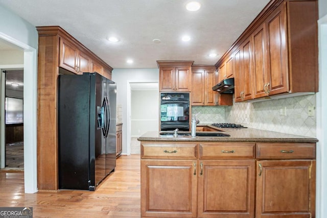 kitchen with under cabinet range hood, backsplash, black appliances, a peninsula, and light wood-style flooring