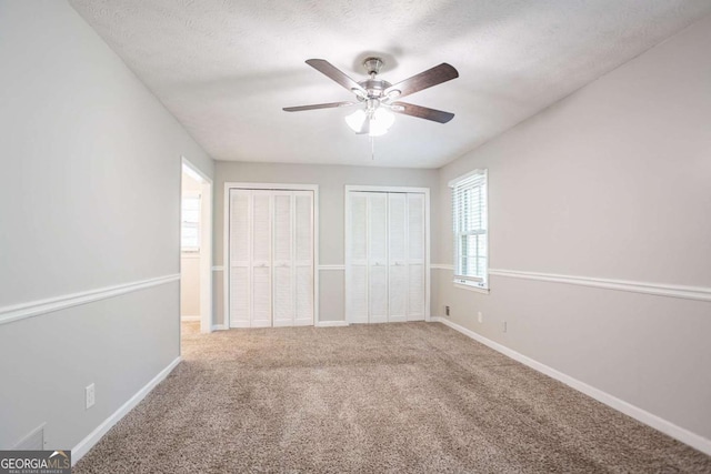 unfurnished bedroom with baseboards, carpet floors, two closets, and multiple windows