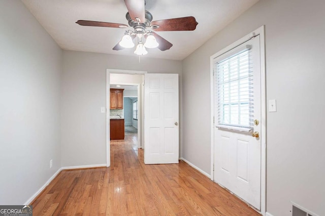 interior space with light wood-type flooring, baseboards, a ceiling fan, and visible vents