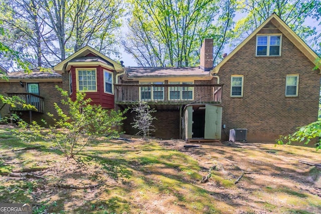 back of property with brick siding, a chimney, central AC unit, and a deck