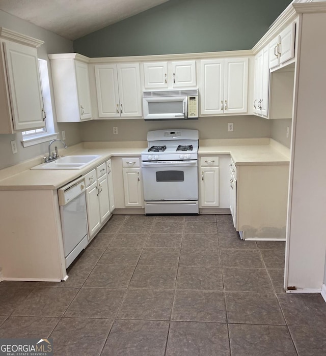 kitchen with white cabinets, a sink, lofted ceiling, white appliances, and dark tile patterned floors