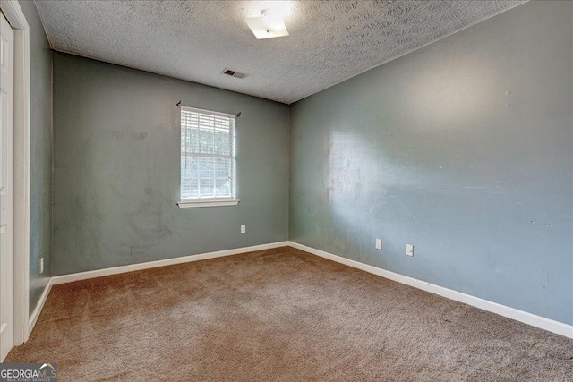 spare room with a textured ceiling, carpet floors, visible vents, and baseboards
