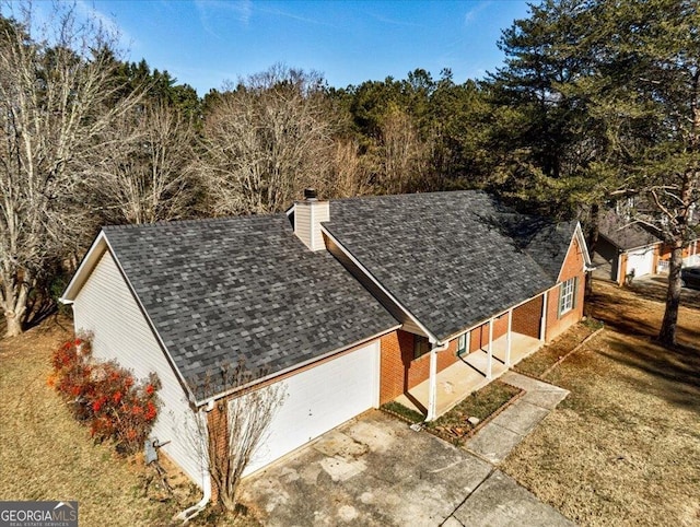 view of property exterior with a chimney, an attached garage, driveway, a lawn, and roof with shingles