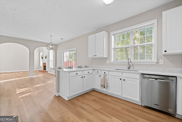 kitchen with arched walkways, dishwasher, a sink, a peninsula, and light wood-style floors