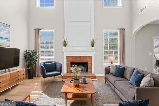 living room with arched walkways, a high ceiling, visible vents, and light wood finished floors