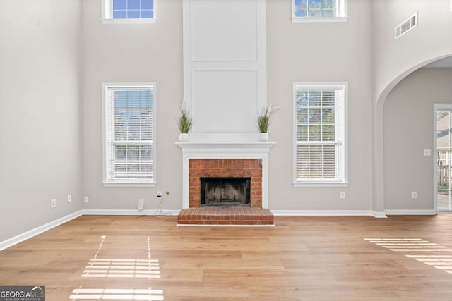 unfurnished living room with arched walkways, visible vents, light wood-style flooring, and a towering ceiling