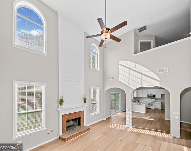 unfurnished living room with visible vents, light wood finished floors, ceiling fan, and a towering ceiling
